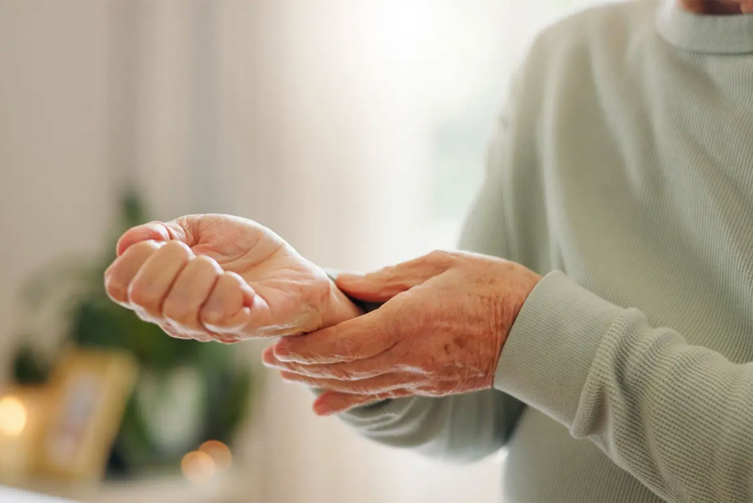 senior man gripping sore wrist indoors utc